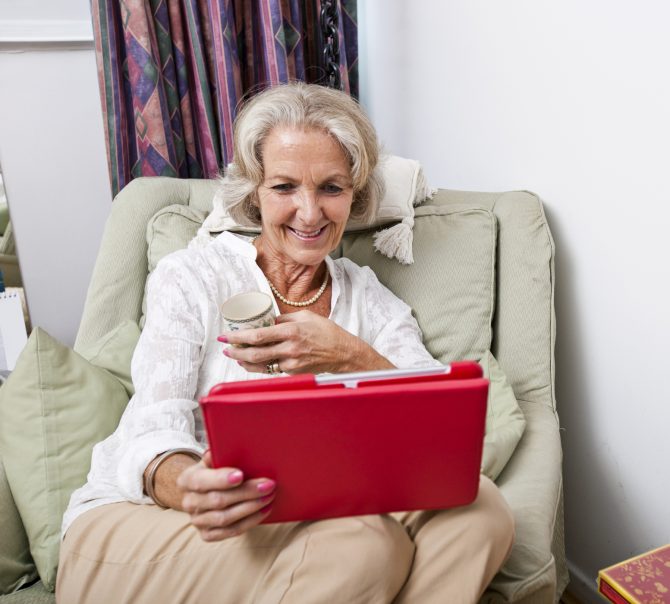 Happy senior woman looking at digital tablet on armchair in house