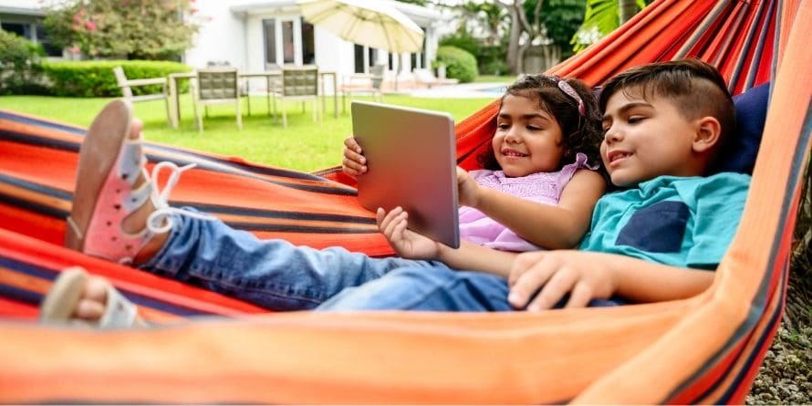 latinx boy and girl children kids reading on a tablet lying in a hammock latinx boy and girl children kids reading on a tablet lying in a hammock